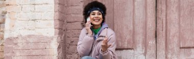 Neşeli Afro-Amerikalı kadın binanın yakınında cep telefonuyla konuşuyor, afiş. 