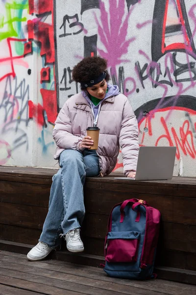 Африканская Американка Кофе Идти Помощью Ноутбука Скамейке Рядом Рюкзак Граффити — стоковое фото