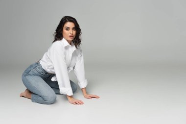 Sensual woman in white shirt kneeling on grey background clipart