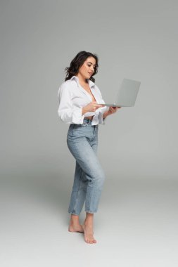 Gülümseyen ve seksi kadın gri arka planda dizüstü bilgisayar kullanıyor. 