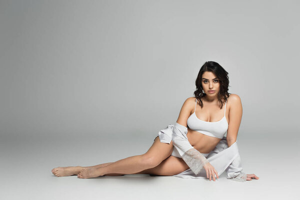 Barefoot woman in underwear and silk robe sitting on grey background 