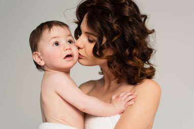 Çıplak omuzlu bir anne, Gri üzerinde izole edilmiş bebeği öpüyor.