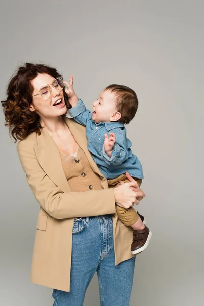 Vrolijk Peuter Jongen Bereiken Bril Krullend Moeder Glimlachen Geïsoleerd Grijs — Stockfoto