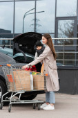 radostná žena drží dítě chlapce v blízkosti auta a nákupní tašky s potravinami