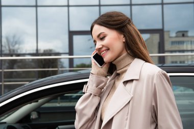 pozitif genç kadın otomobilin yanında akıllı telefondan konuşuyor. 