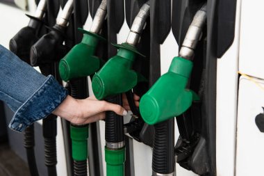 partial view of female hand near gasoline pistols on gas station clipart