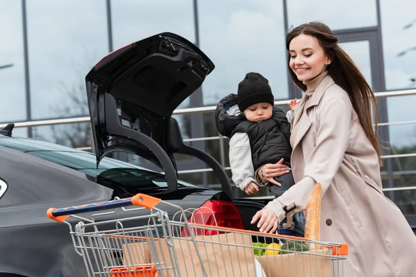 Mãe Feliz Segurando Filho Perto Carro Com Tronco Aberto Carrinho — Fotografia de Stock