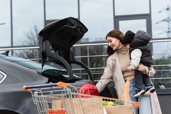 Gelukkig Vrouw Houden Peuter Zoon Buurt Van Auto Kofferbak Winkelwagen — Stockfoto