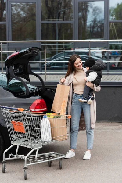 Leende Mor Håller Baby Pojke Nära Bil Och Vagn Med — Stockfoto