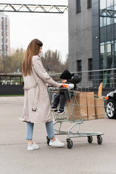 Young Woman Trench Coat Walking Son Purchases Shopping Cart Car — Stock Photo, Image