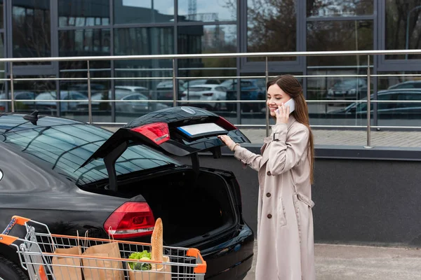 Молодая Женщина Разговаривает Смартфоне Возле Автомобиля Покупки Тележке — стоковое фото