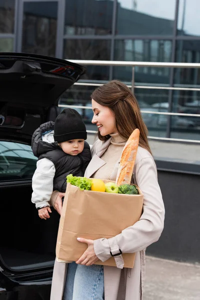 Mujer Sonriente Sosteniendo Niño Bolsa Compras Con Comida Fresca Cerca —  Fotos de Stock