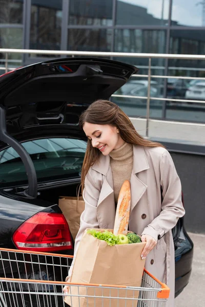 Красивая Улыбающаяся Женщина Держит Сумку Покупками Возле Багажника Машины — стоковое фото