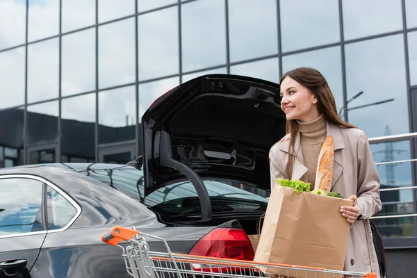 Wanita Bahagia Memegang Tas Belanja Dekat Mobil Dengan Bagasi Terbuka — Stok Foto