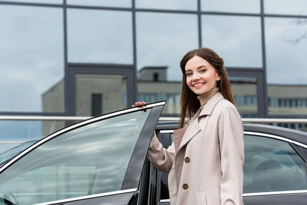 Vacker Kvinna Trenchcoat Ler Mot Kameran Nära Bilen Utomhus — Stockfoto