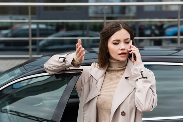 Młoda Kobieta Gestykulując Podczas Rozmowy Przez Telefon Komórkowy Pobliżu Samochodu — Zdjęcie stockowe