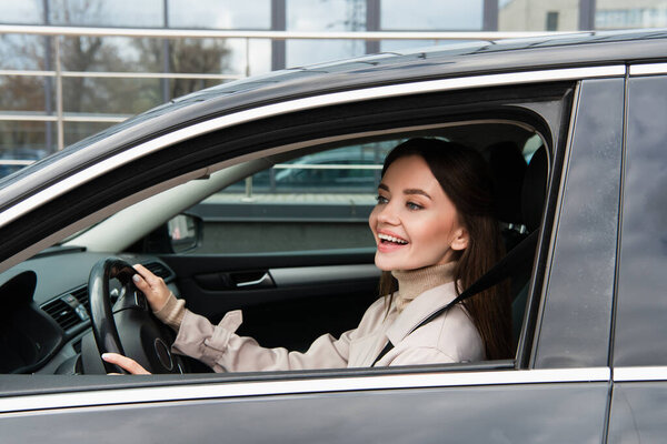 cheerful woman looking out side window while driving car in city