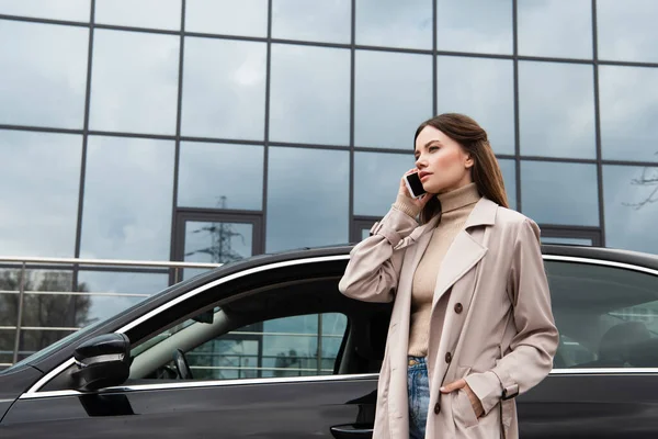 Ung Kvinna Som Håller Hand Fickan Trenchcoat När Talar Smartphone — Stockfoto