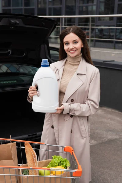 Nöjd Kvinna Håller Flaska Tvättmedel Nära Bil Och Kundvagn — Stockfoto