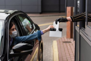 Satıcı arabadaki tıbbi maske takan kadına içecek veriyor.