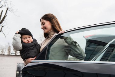 Mutlu anne, dışarıda arabanın yanında küçük çocukla dikiliyor.
