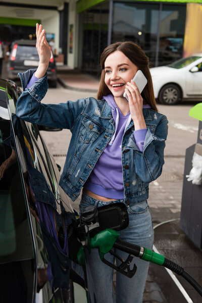 happy woman talking on smartphone while refueling car on gas station