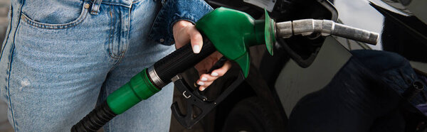 cropped view of woman in jeans fueling car on gas station, banner