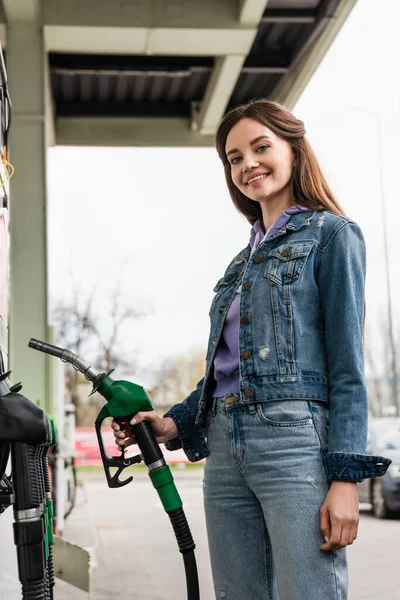 Szczęśliwa Kobieta Patrząc Kamerę Trzymając Pistolet Benzynowy Pobliżu Samochodu — Zdjęcie stockowe