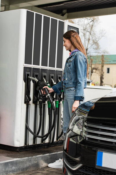 young woman holding gasoline pistol near car on petrol station