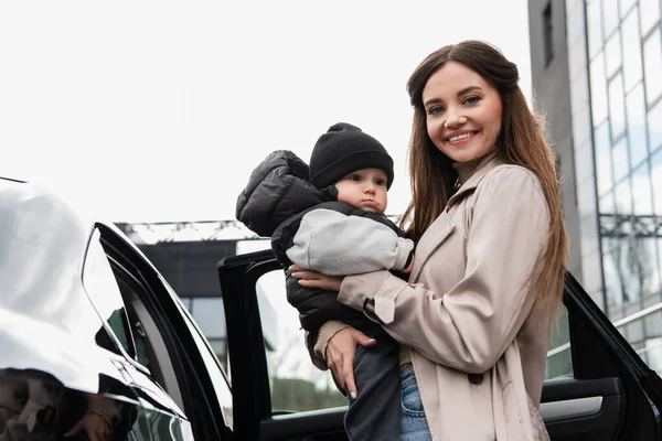 Jolie Femme Souriant Caméra Tout Tenant Petit Enfant Près Voiture — Photo