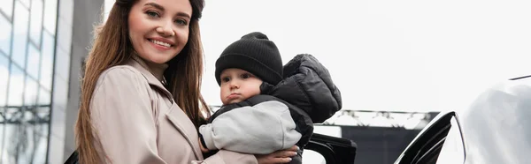 Mujer Sonriendo Cámara Mientras Sostiene Niño Pequeño Aire Libre Pancarta — Foto de Stock