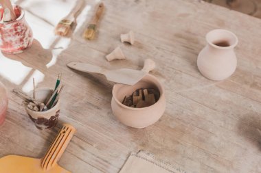 high angle view of handmade clay pots with spatula and pottery equipment on wooden table