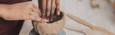 partial view of young african american woman sculpting clay pot with hands in pottery, banner