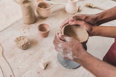 partial view of young african american couple sculpting clay pot with holding hands together in pottery