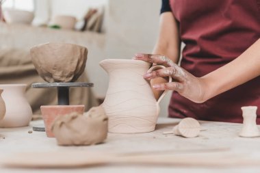 partial view of young african american woman touching clay pot in pottery