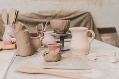 handmade pots, sculpted clay bowl and pottery equipment on wooden table 
