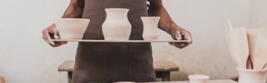 partial view of young african american man standing with clay pots on tray, banner