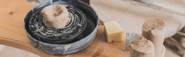 high angle view of wet piece of clay on pottery wheel and sponge on wooden bench in art studio, banner