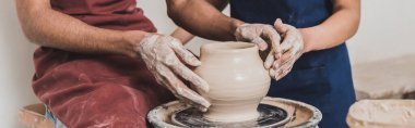 partial view of young african american couple modeling wet clay pot on wheel with hands in pottery, banner