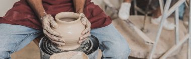 partial view of young african american man making wet clay pot on wheel in pottery, banner