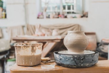 sculpted wet clay pot on pottery wheel on wooden table in art studio