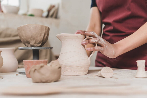 partial view of young african american woman touching clay pot in pottery