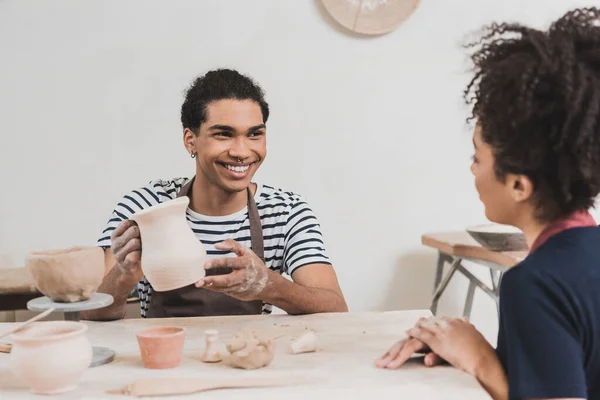 Sorridente Jovem Afro Americano Homem Mostrando Pote Barro Para Mulher — Fotografia de Stock