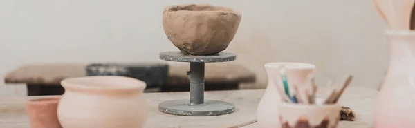 sculpted clay bowl on wooden table in pottery art studio, banner