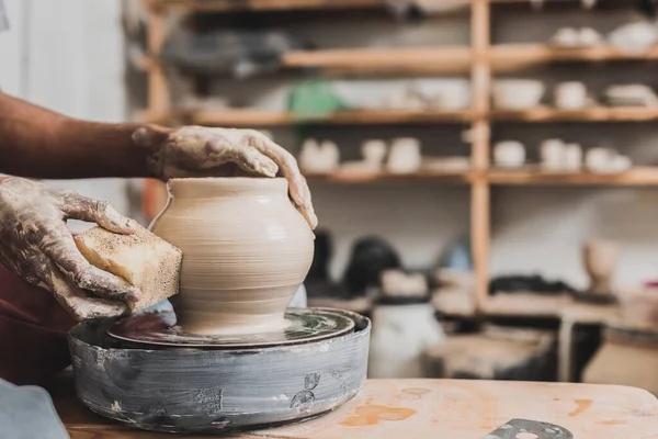 スポンジを手にしたアフリカ系アメリカ人の若者が陶器の車輪にぬれた土鍋を作っている様子がよく見えます — ストック写真