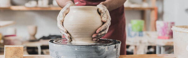 partial view of young african american man making wet clay pot on wheel with hands in pottery, banner