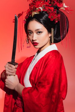 Geleneksel kimonolu Asyalı kadın kırmızı arka planda kılıç tutuyor. 