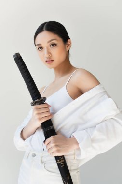 Young japanese woman holding sheath of sword isolated on grey clipart