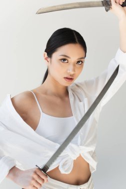 Beyaz tişörtlü genç Japon kadın gri üzerinde izole edilmiş kılıçlar tutuyor.