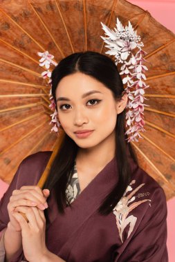 Japanese woman in kimono holding umbrella on blurred background isolated on pink  clipart